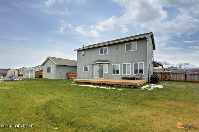 rear view of property with a lawn, a deck with mountain view, and a storage shed