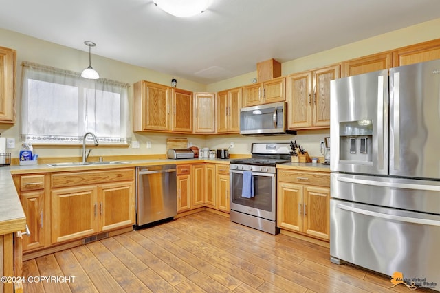 kitchen with light wood-type flooring, appliances with stainless steel finishes, sink, and hanging light fixtures