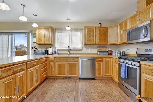 kitchen featuring sink, light wood-type flooring, appliances with stainless steel finishes, and decorative light fixtures