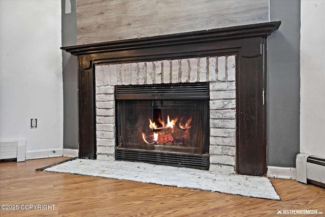 room details with a baseboard heating unit, hardwood / wood-style flooring, and a fireplace