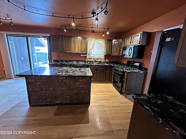 kitchen featuring dark stone counters, black appliances, sink, light wood-type flooring, and a kitchen island