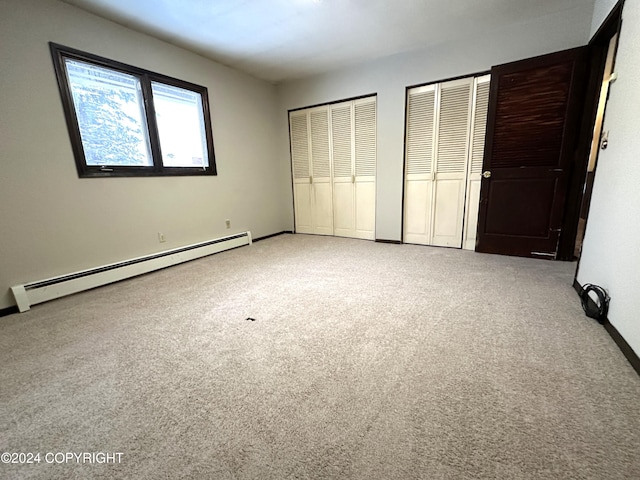 unfurnished bedroom with carpet flooring, a baseboard radiator, and two closets