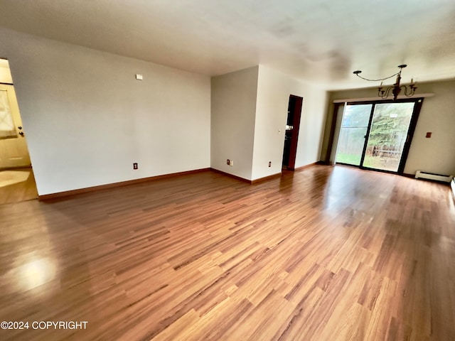 unfurnished room with a notable chandelier, light wood-type flooring, and a baseboard radiator