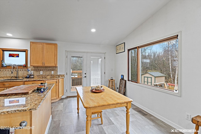 kitchen with light stone counters, vaulted ceiling, sink, and light brown cabinets