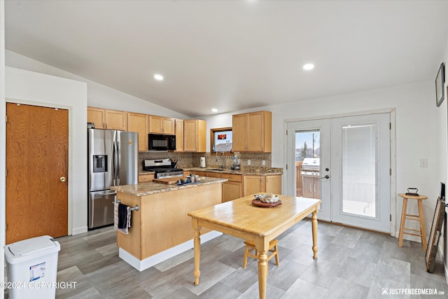 kitchen with lofted ceiling, light stone countertops, a center island, stainless steel appliances, and sink