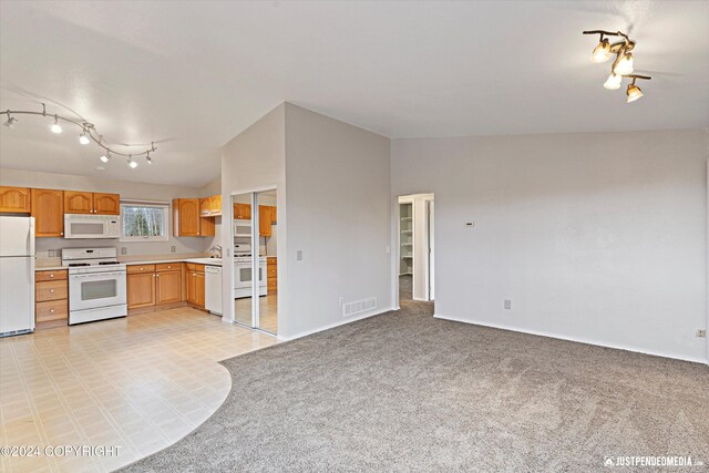 kitchen with white appliances, sink, vaulted ceiling, track lighting, and light colored carpet