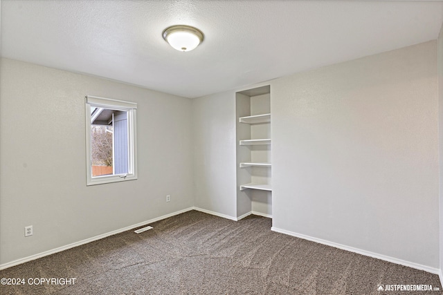 unfurnished bedroom with dark carpet and a textured ceiling