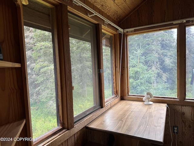 unfurnished sunroom featuring vaulted ceiling, wood walls, and a wealth of natural light