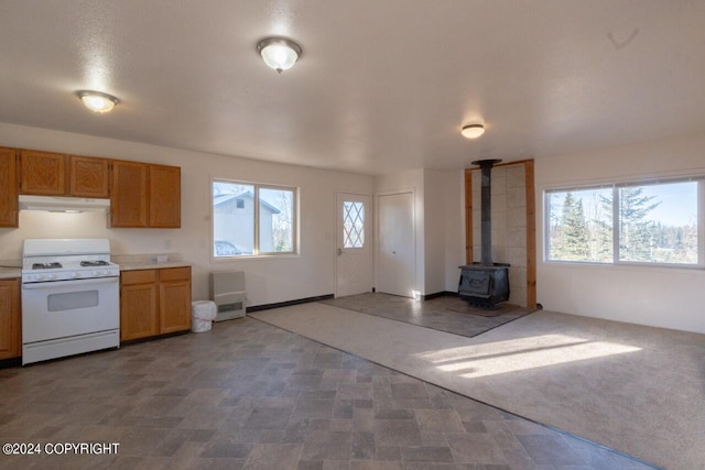 kitchen with a healthy amount of sunlight, dark carpet, white gas range, and a wood stove