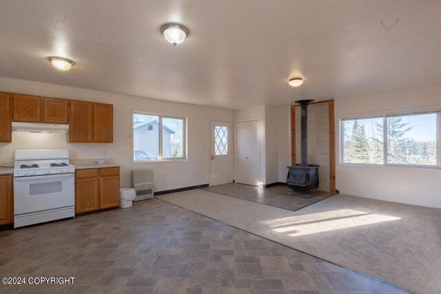 65449 Lingonberry Rd, Ninilchik, AK 99639 - kitchen with white range with gas stovetop, brown cabinets, light countertops, under cabinet range hood, and a wood stove