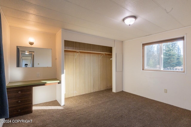 unfurnished bedroom with a closet, built in desk, and carpet floors