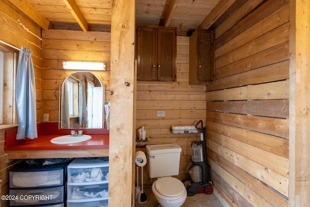 bathroom featuring toilet, beamed ceiling, wooden ceiling, sink, and wood walls