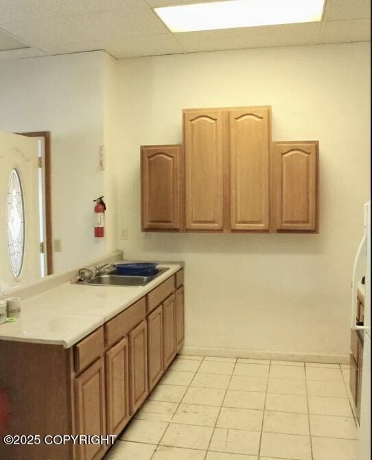 kitchen featuring light countertops, a drop ceiling, a sink, and light tile patterned flooring