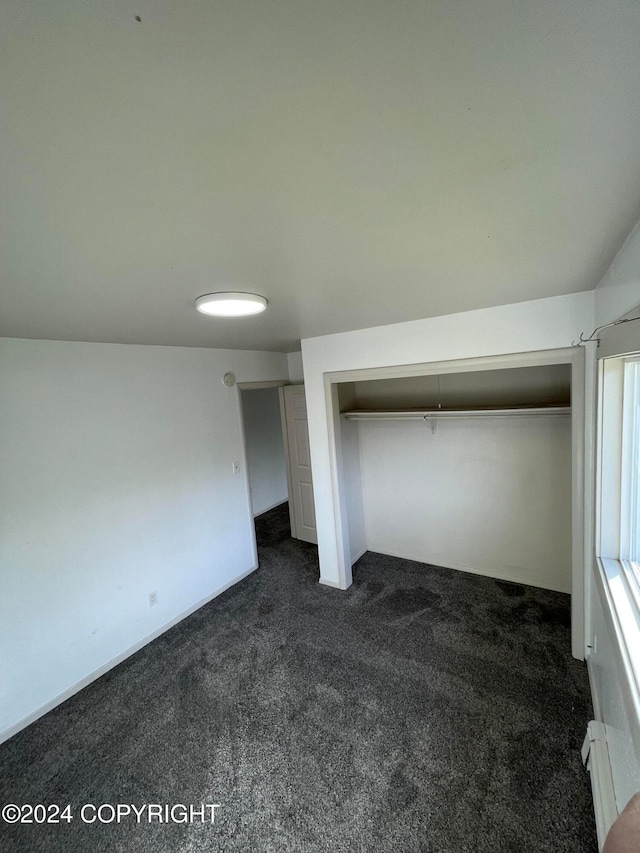 unfurnished bedroom with a closet, baseboard heating, and dark colored carpet