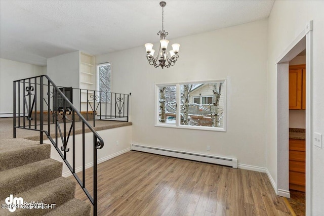 stairs featuring a notable chandelier, a textured ceiling, baseboard heating, and hardwood / wood-style floors