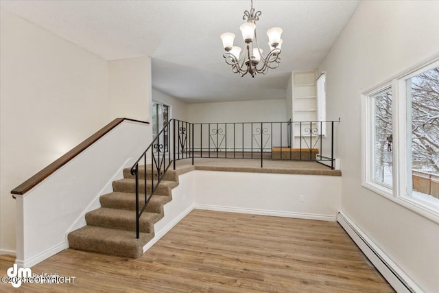 staircase featuring hardwood / wood-style flooring, a chandelier, a baseboard radiator, and a wealth of natural light