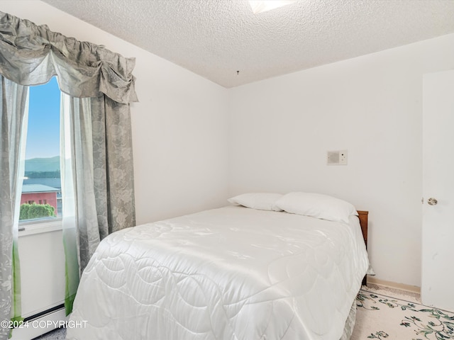 bedroom with a textured ceiling, a water view, and a baseboard heating unit