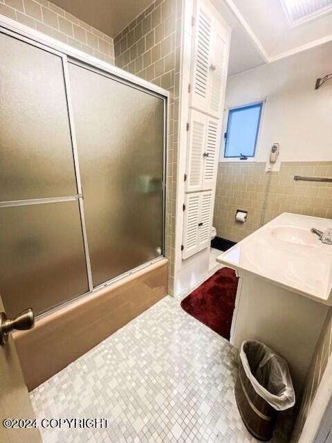 bathroom featuring tile patterned flooring, vanity, enclosed tub / shower combo, and tile walls