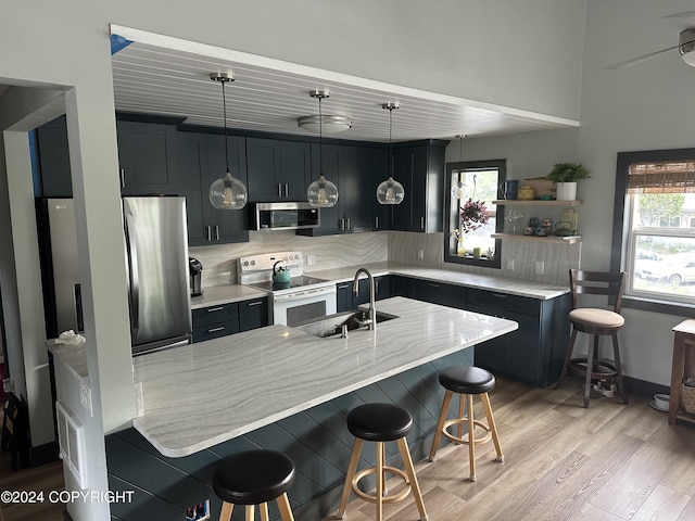 kitchen featuring sink, stainless steel appliances, light hardwood / wood-style flooring, pendant lighting, and a breakfast bar area