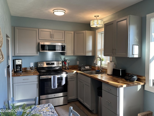 kitchen featuring gray cabinetry, stainless steel appliances, sink, butcher block countertops, and hanging light fixtures