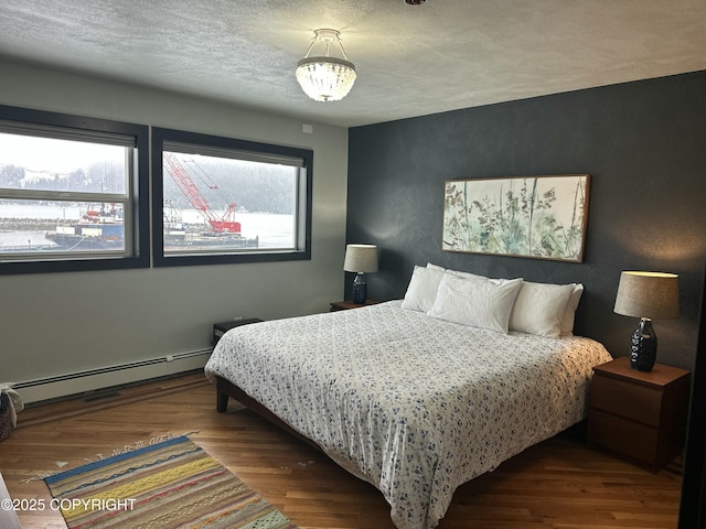 251 Main St, Seldovia, AK 99663 - bedroom featuring baseboard heating, a textured ceiling, wood finished floors, and an inviting chandelier