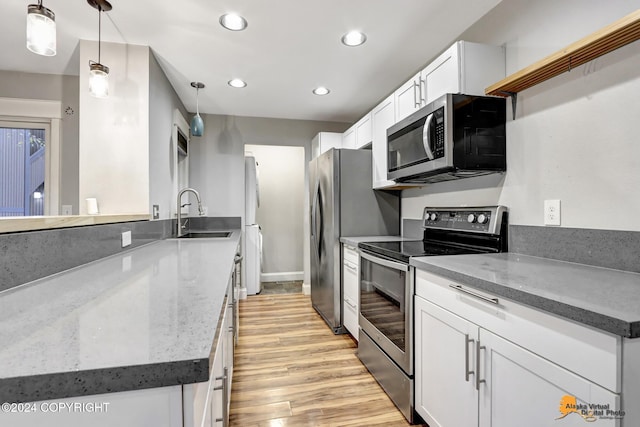 kitchen featuring hanging light fixtures, stainless steel appliances, sink, white cabinetry, and light hardwood / wood-style floors