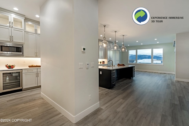 kitchen with a center island with sink, wine cooler, stainless steel microwave, white cabinets, and pendant lighting