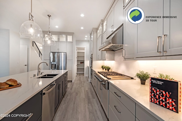 kitchen featuring light hardwood / wood-style floors, sink, light stone counters, appliances with stainless steel finishes, and hanging light fixtures