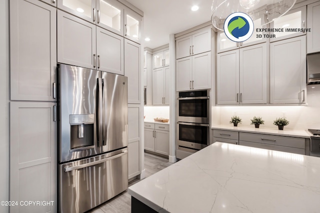 kitchen featuring light stone counters, appliances with stainless steel finishes, gray cabinetry, light wood-type flooring, and decorative backsplash