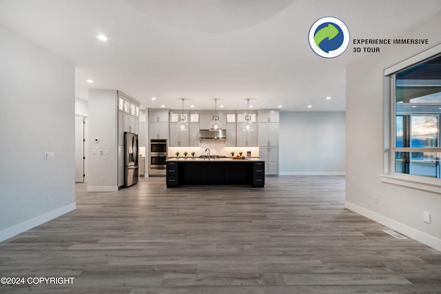 kitchen with pendant lighting, stainless steel appliances, wood-type flooring, and a center island with sink