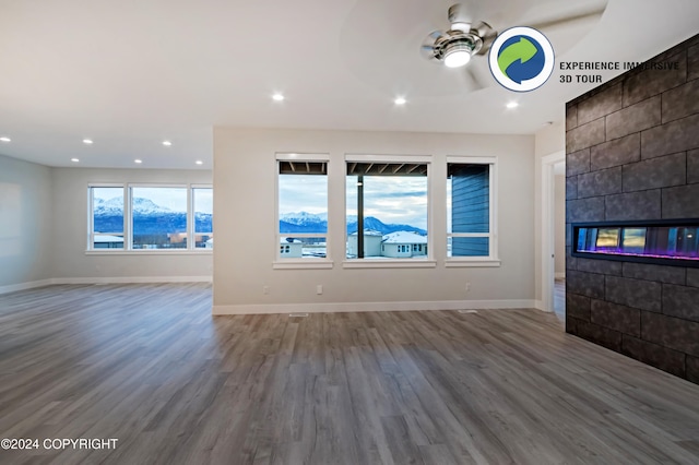 unfurnished living room featuring ceiling fan, hardwood / wood-style flooring, and a tiled fireplace