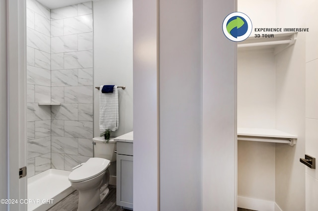 bathroom featuring a tile shower, wood-type flooring, toilet, and vanity