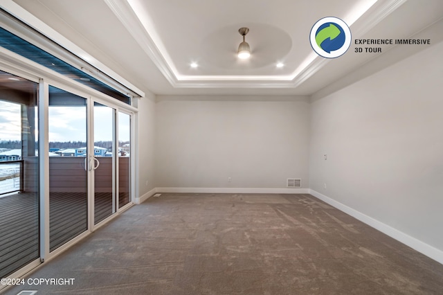 spare room with dark colored carpet, a raised ceiling, and crown molding