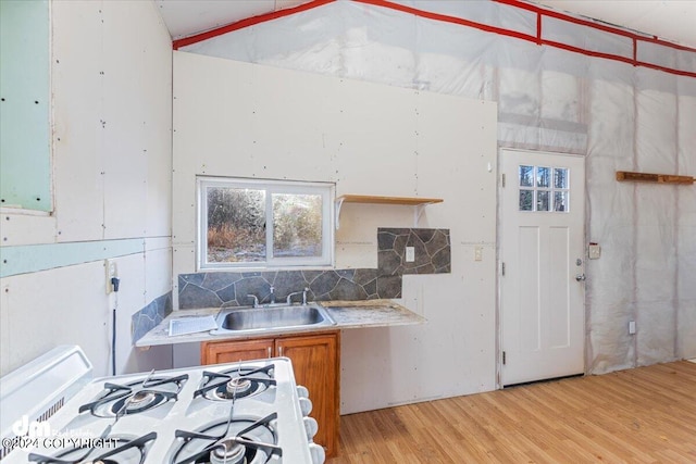 kitchen featuring white range with gas stovetop, backsplash, sink, and light hardwood / wood-style floors