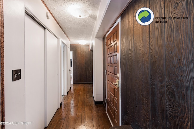 corridor featuring dark hardwood / wood-style flooring, a textured ceiling, and wooden walls