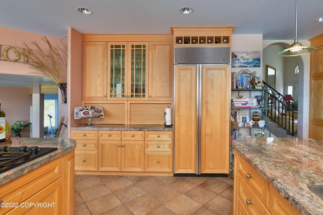 kitchen with paneled fridge, light brown cabinets, light stone countertops, and black stovetop