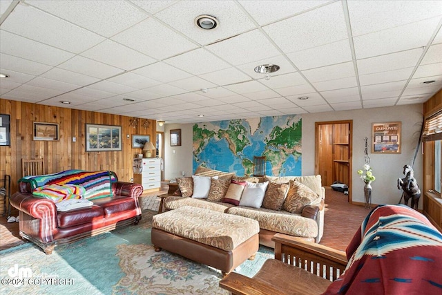 living room featuring carpet flooring, a paneled ceiling, and wooden walls