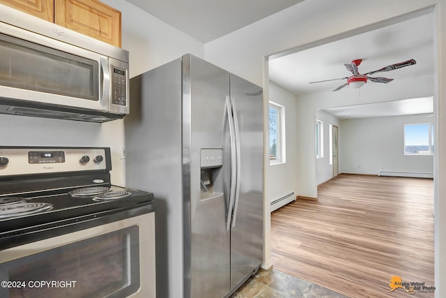 kitchen featuring appliances with stainless steel finishes, a baseboard heating unit, light brown cabinetry, and light hardwood / wood-style floors