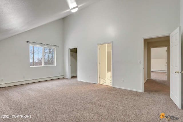 unfurnished bedroom with a baseboard heating unit, a spacious closet, carpet flooring, ensuite bathroom, and high vaulted ceiling