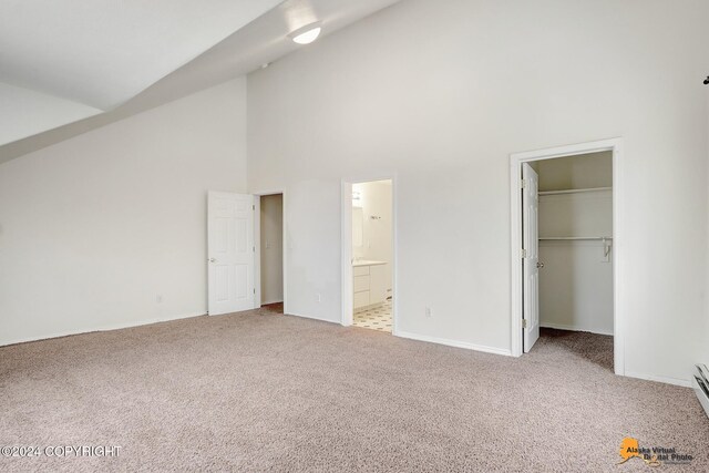 unfurnished bedroom with a spacious closet, ensuite bathroom, high vaulted ceiling, and light colored carpet