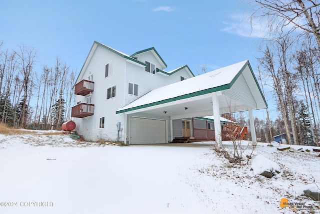 snow covered rear of property with a balcony and a garage