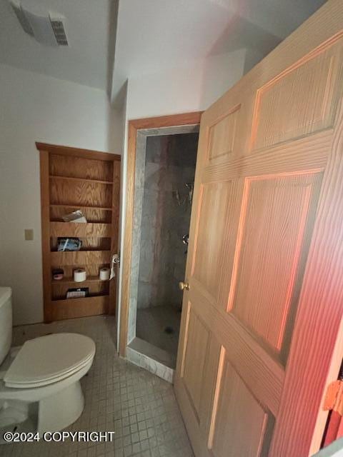 bathroom featuring a tile shower, toilet, and tile patterned flooring