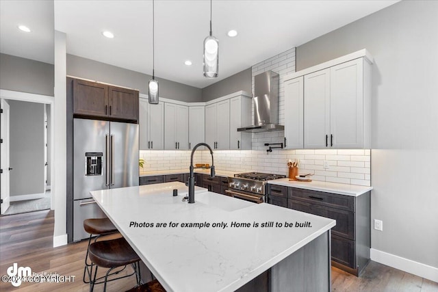 kitchen with sink, hanging light fixtures, premium appliances, an island with sink, and wall chimney exhaust hood