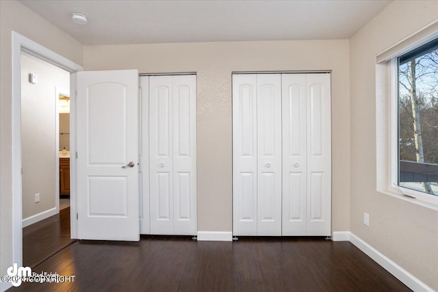 unfurnished bedroom with two closets and dark wood-type flooring