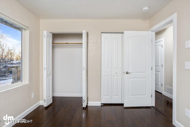 unfurnished bedroom with dark wood-type flooring and two closets