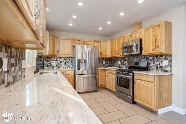 kitchen with appliances with stainless steel finishes, tasteful backsplash, sink, and light stone counters