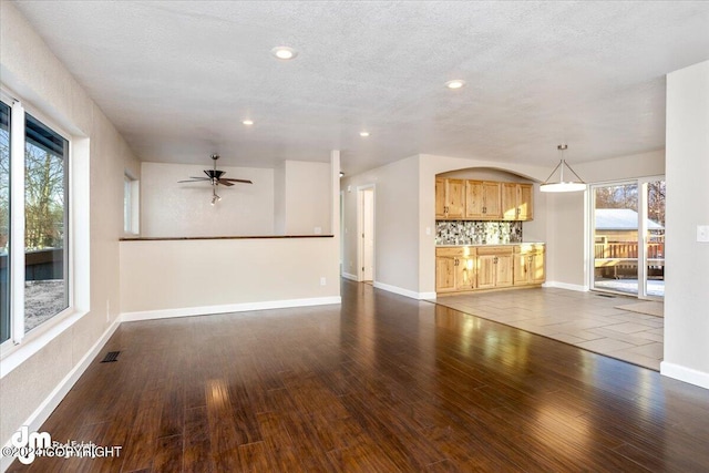 unfurnished living room featuring a textured ceiling, dark hardwood / wood-style floors, and a healthy amount of sunlight