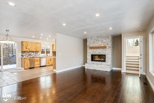 unfurnished living room with a stone fireplace, a textured ceiling, and light wood-type flooring