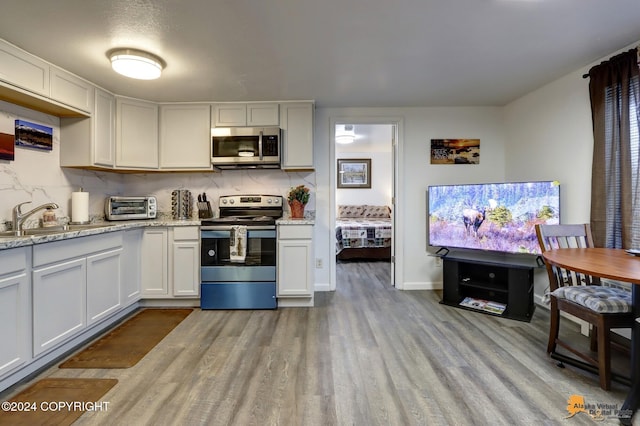 kitchen featuring appliances with stainless steel finishes, light stone countertops, sink, white cabinets, and light hardwood / wood-style flooring