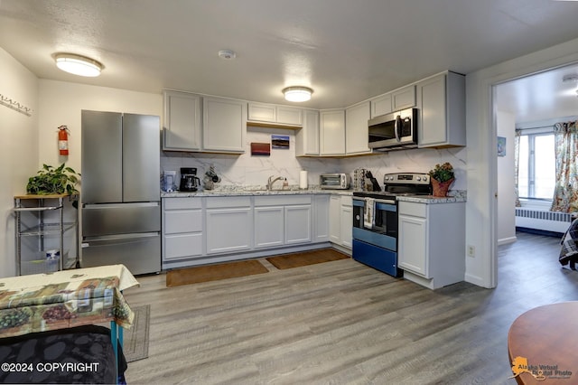 kitchen with radiator heating unit, light hardwood / wood-style flooring, backsplash, white cabinetry, and appliances with stainless steel finishes